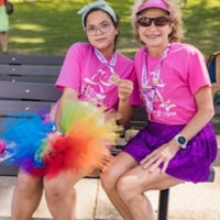 A Girls on the Run coach and girl participant smiles while holding a program medal at the 5K